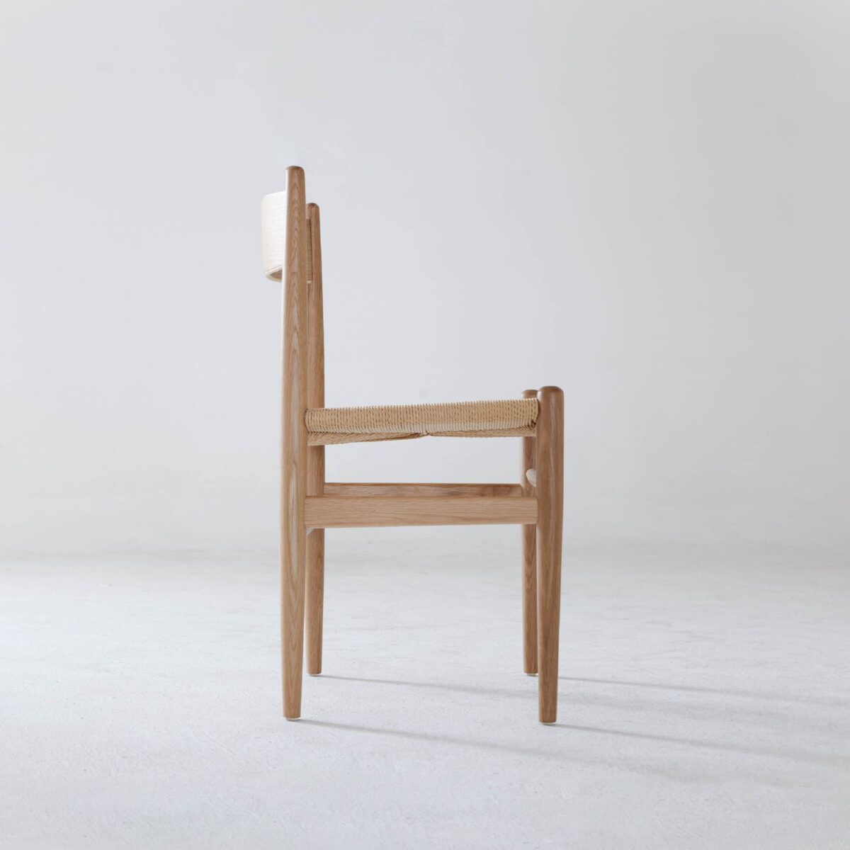 CH36 Chair_B8 A minimalist wooden chair with a woven seat is shown in side view against a plain white background. The chair has clean lines and a simple, modern design.