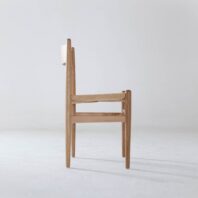A minimalist wooden chair with a woven seat is shown in side view against a plain white background. The chair has clean lines and a simple, modern design.