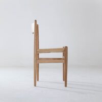 A minimalist wooden chair with a woven seat is shown in side view against a plain white background. The chair has clean lines and a simple, modern design.