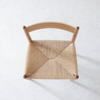 Top view of a wooden chair with a curved backrest and a woven, natural fibre seat, placed on a light, textured surface.