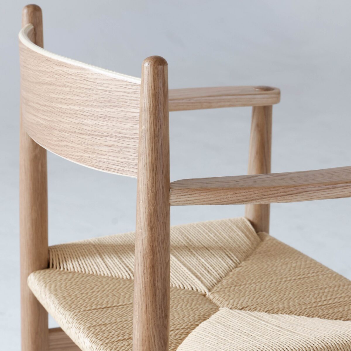 CH37_B4 A close-up of a modern wooden chair with a curved backrest and woven seat, featuring light-coloured wood and minimalist Scandinavian design elements.