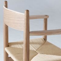 A close-up of a modern wooden chair with a curved backrest and woven seat, featuring light-coloured wood and minimalist Scandinavian design elements.