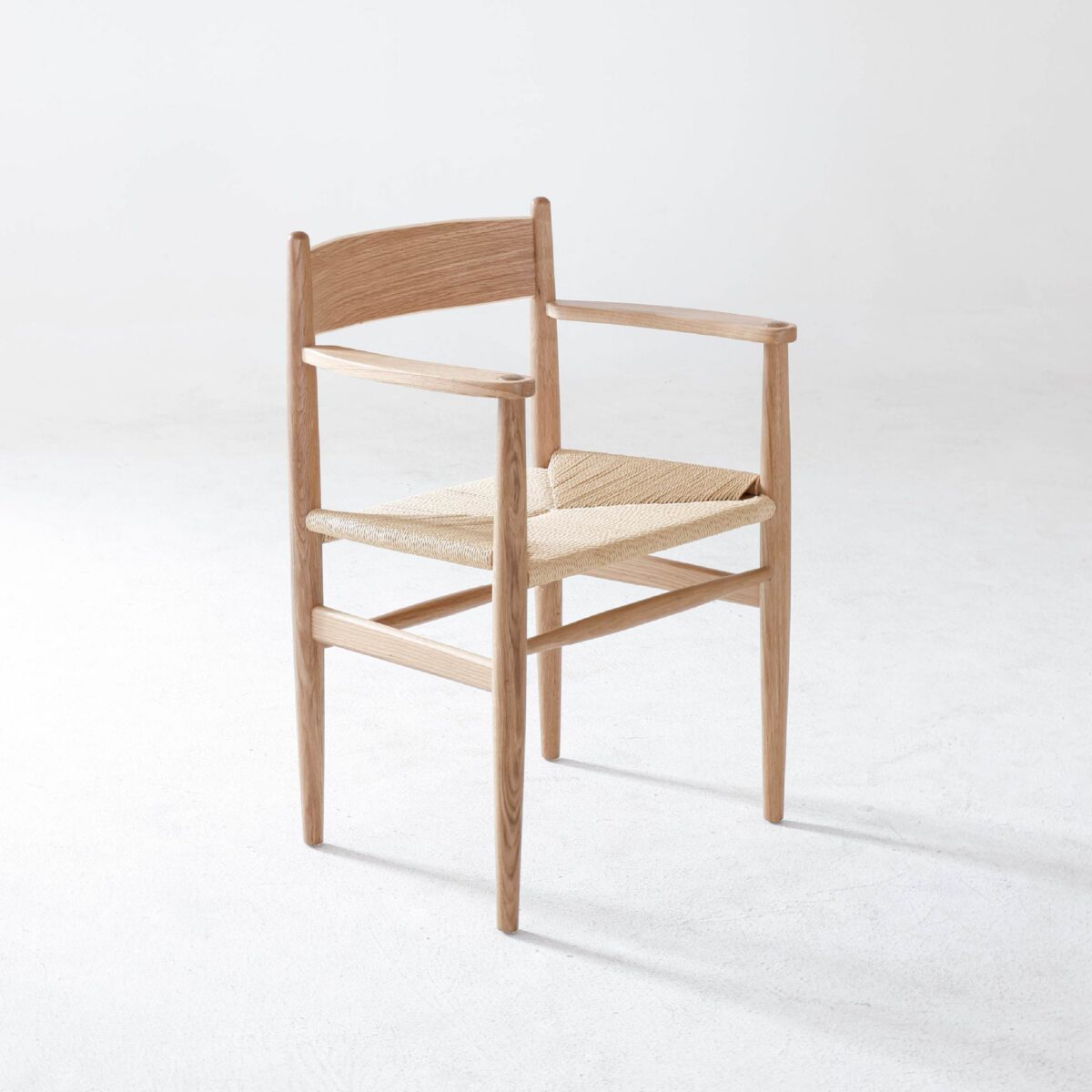 CH37_B6 A minimalist wooden chair with a woven seat, slender legs, and armrests, set against a plain white background.