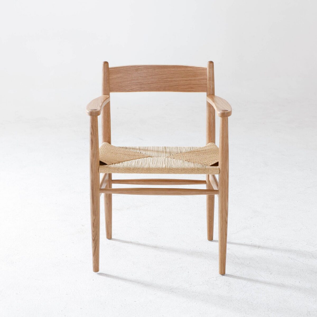 CH37_B7 A wooden armchair with a natural finish and a woven seat is positioned on a light, textured floor against a plain white background.