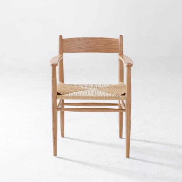 A wooden armchair with a natural finish and a woven seat is positioned on a light, textured floor against a plain white background.