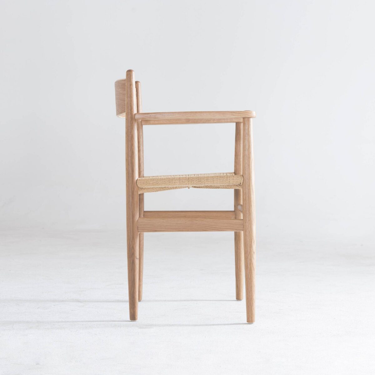 CH37_B8 A side view of a wooden chair with armrests and a woven seat, set against a plain white background.