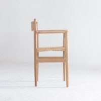A side view of a wooden chair with armrests and a woven seat, set against a plain white background.