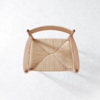 Top-down view of a wooden chair with a woven natural fibre seat, set against a plain white background. The chair has curved wooden armrests and a simple, minimalist design.