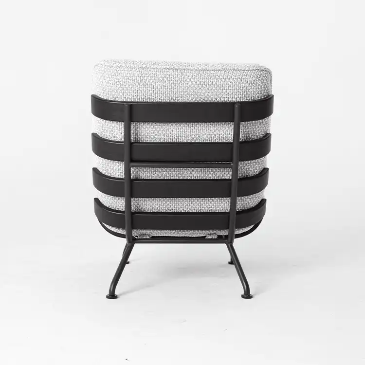 Contemporary accent chair viewed from the back, featuring a light grey textured cushion and a black metal frame with horizontal slats and slender legs, set against a plain white background.