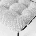 Close-up of a tufted, textured light grey fabric cushion on a black metal chair leg, showing the detailed weave and soft padding.