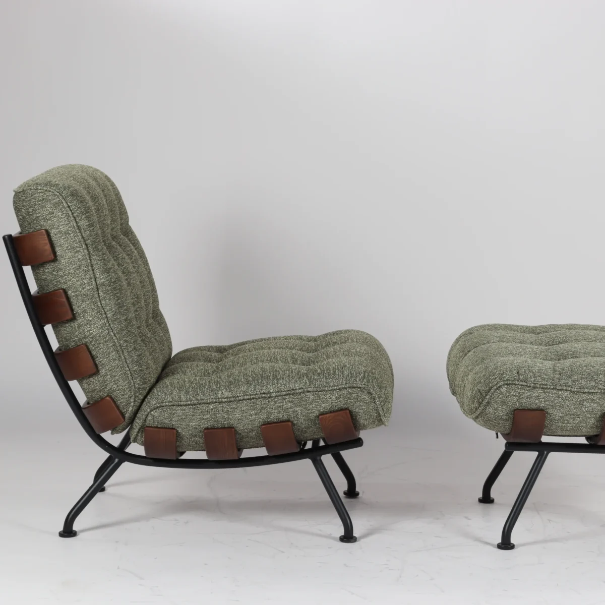 Costela Chair_Green Set_Side View A modern lounge chair with matching ottoman, both featuring textured green cushions, black metal frames, and brown leather straps along the sides. The background is plain white.