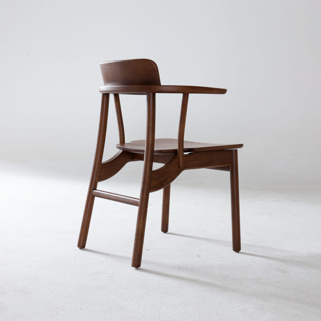 A modern wooden chair with a curved backrest and armrests, positioned on a plain white background. The design is minimalist, featuring smooth, clean lines and a natural wood finish.