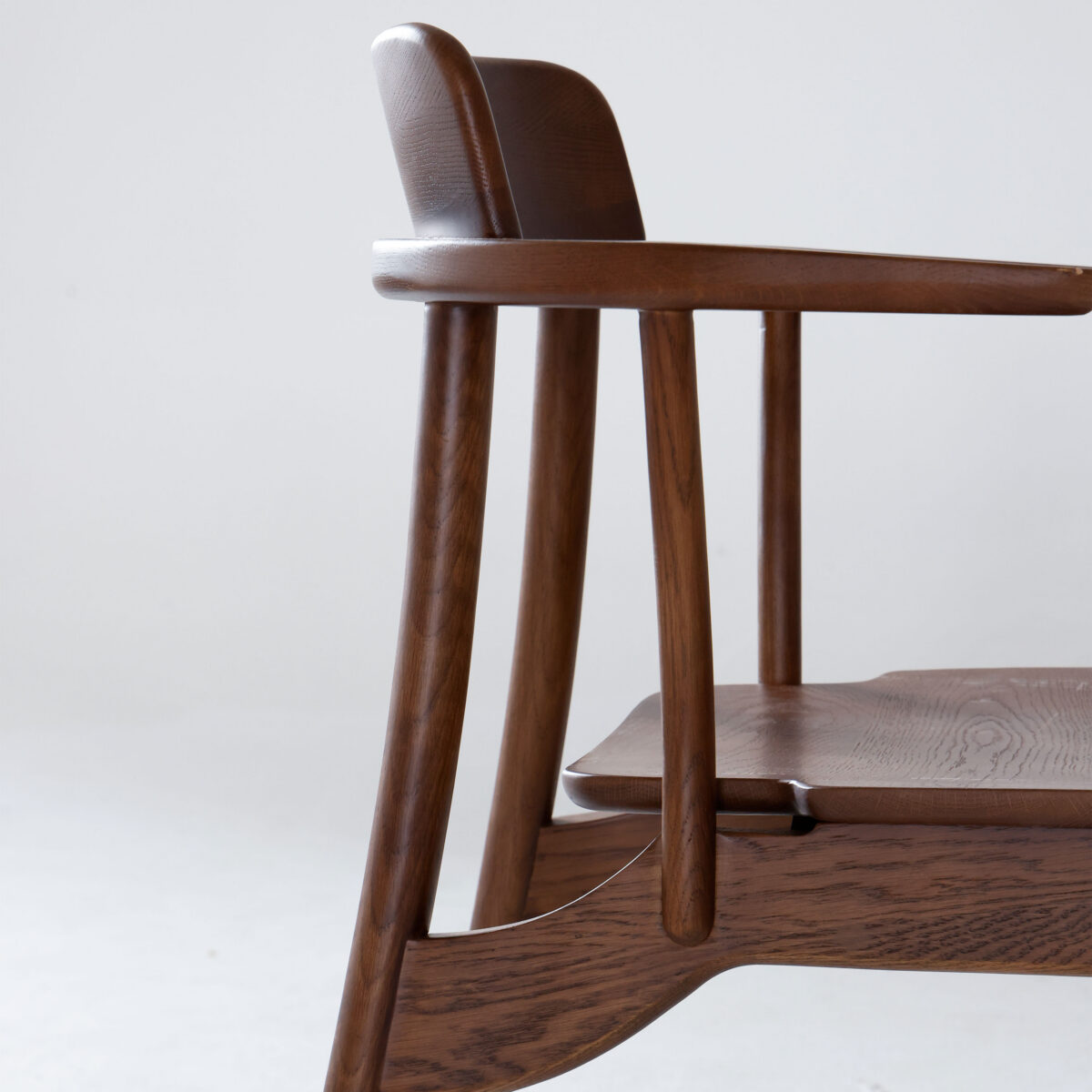 Crown Chair_Dark Brown_B6 Side view of a modern wooden chair with curved armrests, a slightly reclined backrest, and a smooth, polished finish against a plain light background.