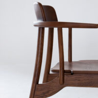 Side view of a modern wooden chair with curved armrests, a slightly reclined backrest, and a smooth, polished finish against a plain light background.