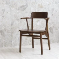 A wooden chair with curved armrests and backrest sits on a light tiled floor against a stone wall backdrop.
