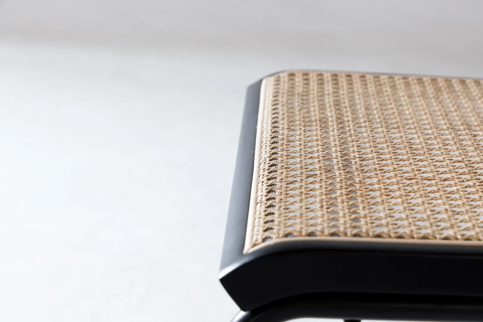 Detail display1 Close-up of the corner of a woven rattan seat with a black wooden frame, set against a plain light background.