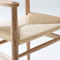 A close-up of a wooden chair with a woven natural fibre seat, showing detailed craftsmanship in the weaving and smooth light wood frame.