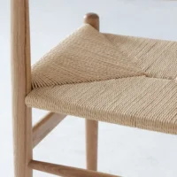 Close-up of a wooden chair with a woven natural fibre seat, showcasing its geometric pattern and light wood frame against a plain, light background.