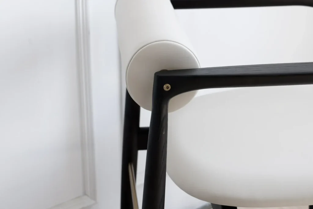 Close-up of a modern chair with a black wooden frame and white cylindrical cushion for the backrest, paired with a round white seat cushion, set against a white background.