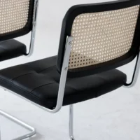 Two modern chairs with chrome frames, black cushioned seats, and woven cane backs are positioned on a light-coloured floor. The design is minimalist and contemporary.