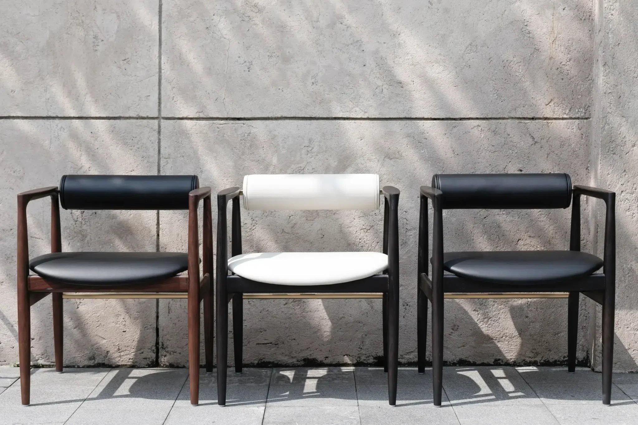 Three Quokka dining chairs in brown, black colour timbers, in black and white colour leather. Cement wall background.