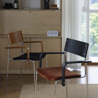 Two dining chairs with timber and black details, steel legs and frame, styled in a living space with a light wood cabinet and large window.