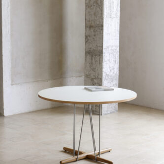 Modern round dining table with a white tabletop, slender metal legs and a timber cross-base, shown in a minimal interior.