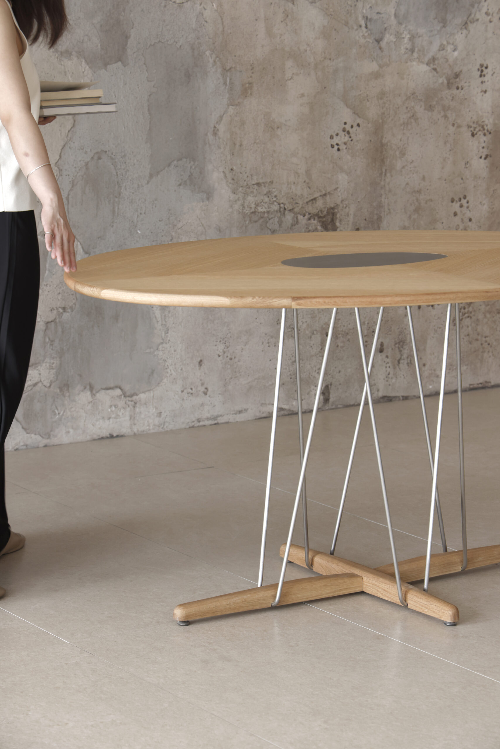 Pebble Dining Table Close-up image of rounded wooden dining table, sculptural metal legs and timber top against concrete wall.