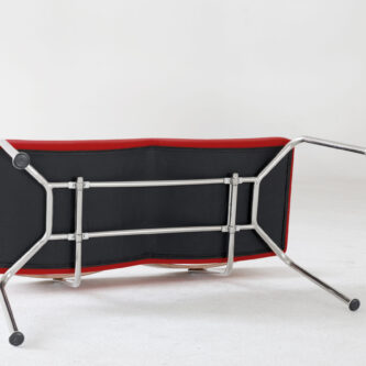 Underside view of a red modern bench seat showing metal frame and support structure, shown on a plain white background.