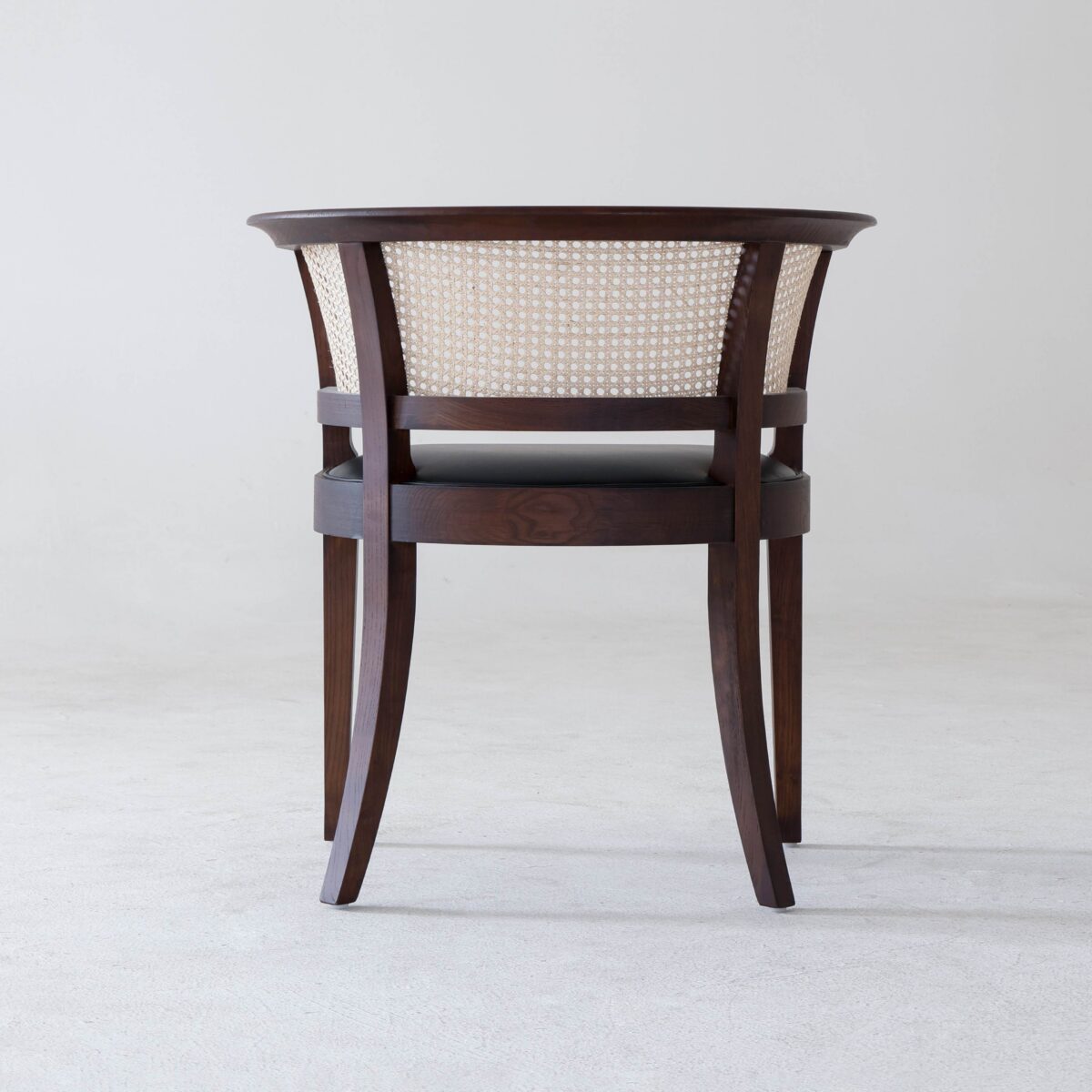 Faaborg Chair_B2 A wooden chair with a curved backrest and woven cane panel, viewed from behind, standing on a light-coloured floor against a plain white background.