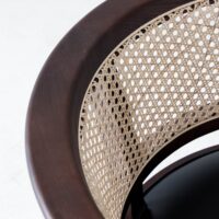 Close-up of a chair with a curved dark wood frame and a woven cane backrest, showcasing the detailed pattern and texture of the cane against the smooth wood.
