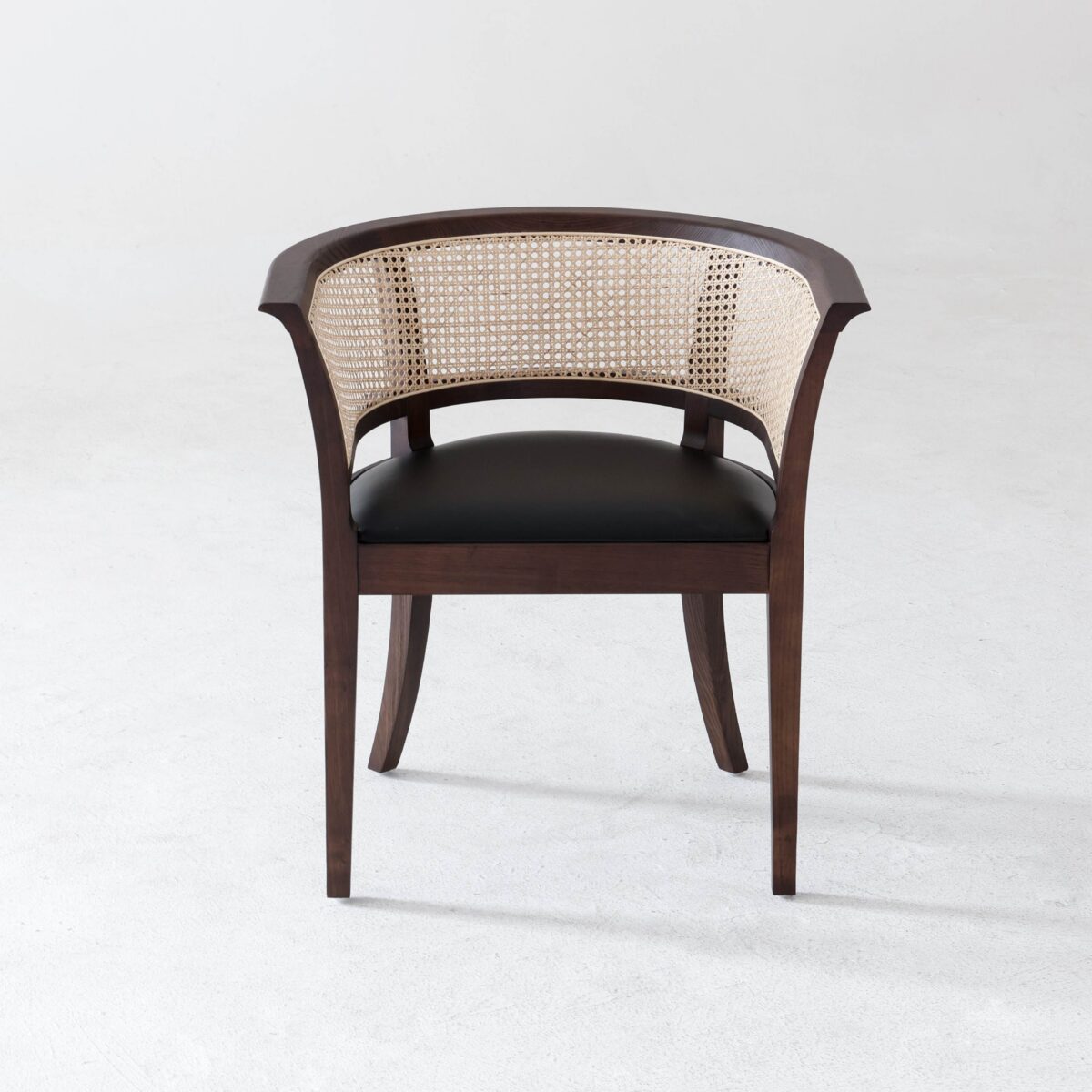 Faaborg Chair_B6 A wooden chair with a curved cane backrest, dark brown frame, and black cushioned seat, placed on a light, minimalist floor background.