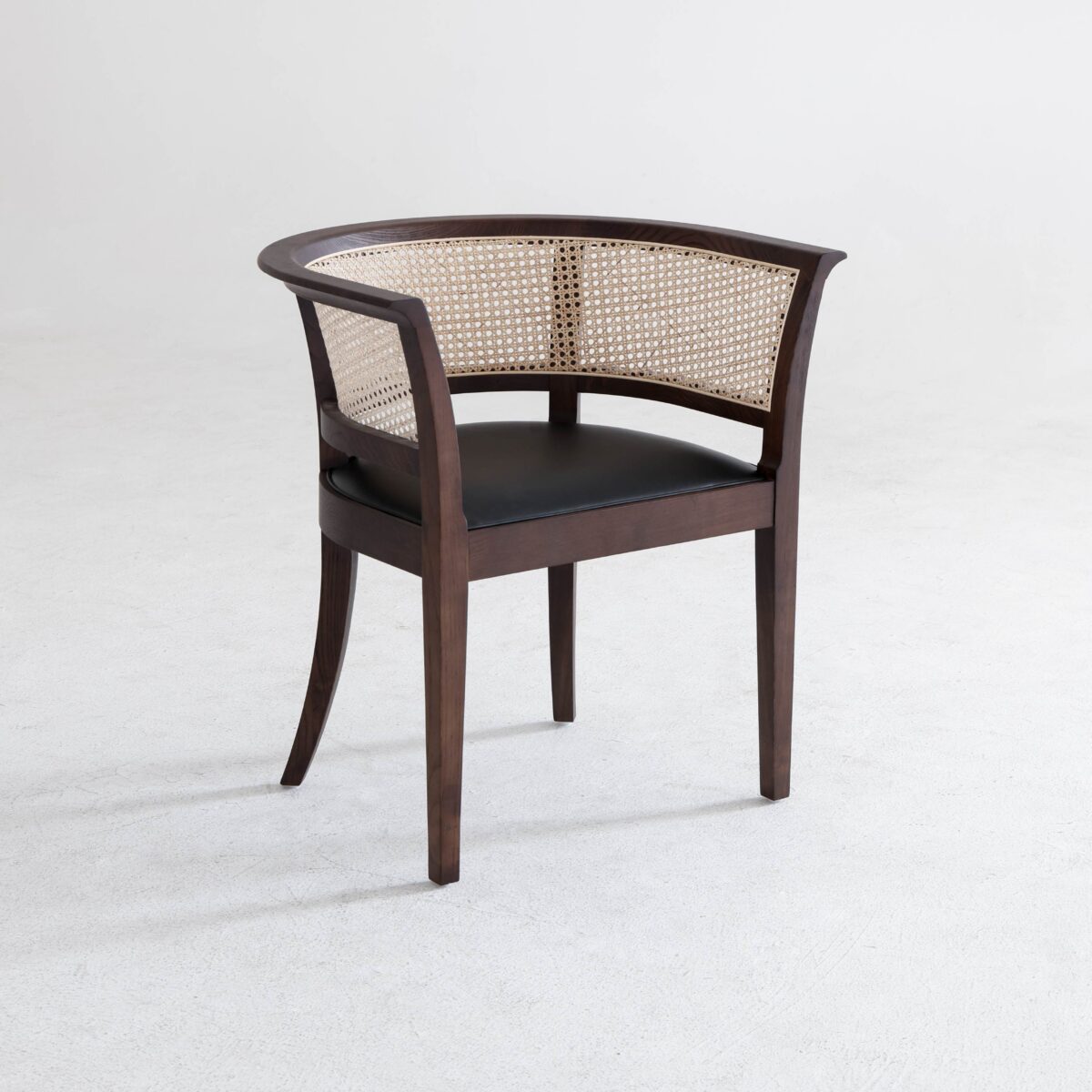Faaborg Chair_B7 A wooden chair with a curved backrest featuring woven cane, dark brown frame, and a black cushioned seat, set on a light grey floor against a plain white background.