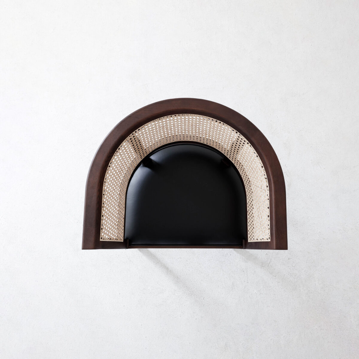 Faaborg Chair_B9 A top-down view of a modern chair with a black seat, a curved wooden frame, and woven cane backrest, placed on a light textured surface.