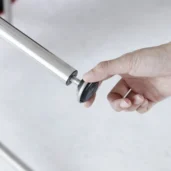 A hand is screwing a round, black-and-silver adjustable foot into the end of a metal tube, likely assembling furniture.