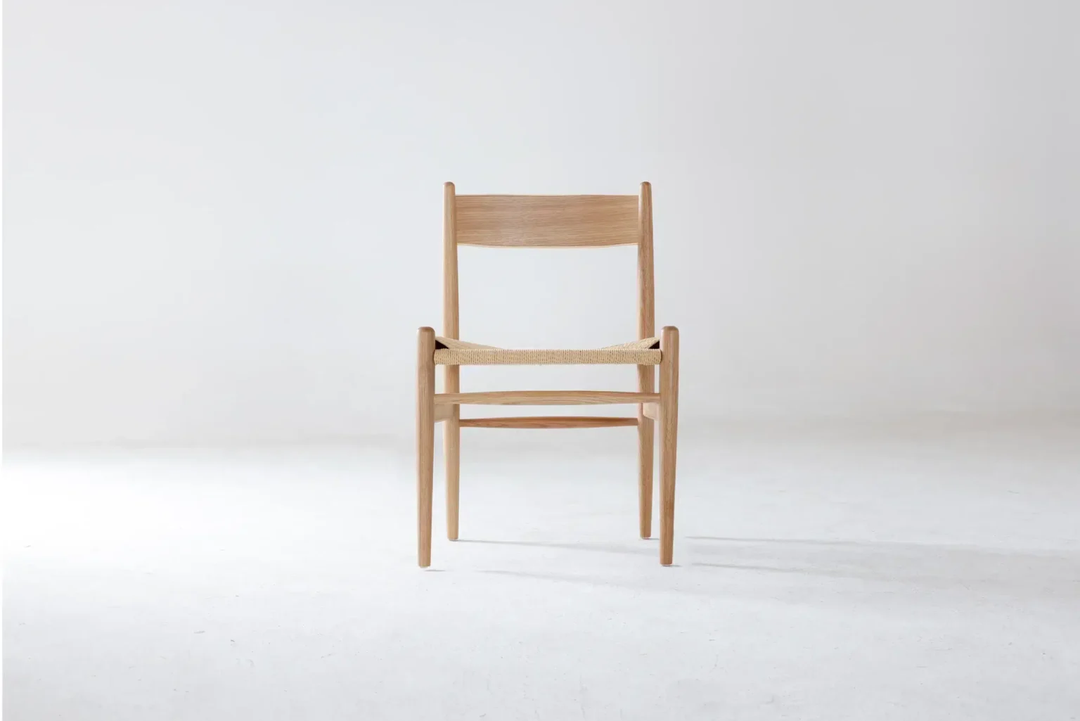 Front view A simple wooden chair with a woven seat is centred against a plain white background, viewed from the front. The design is minimalist and modern.