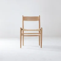 A simple wooden chair with a woven seat is centred against a plain white background, viewed from the front. The design is minimalist and modern.