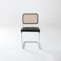 A single chair with a woven cane backrest, black cushioned seat, and metal legs is centred against a plain white background.