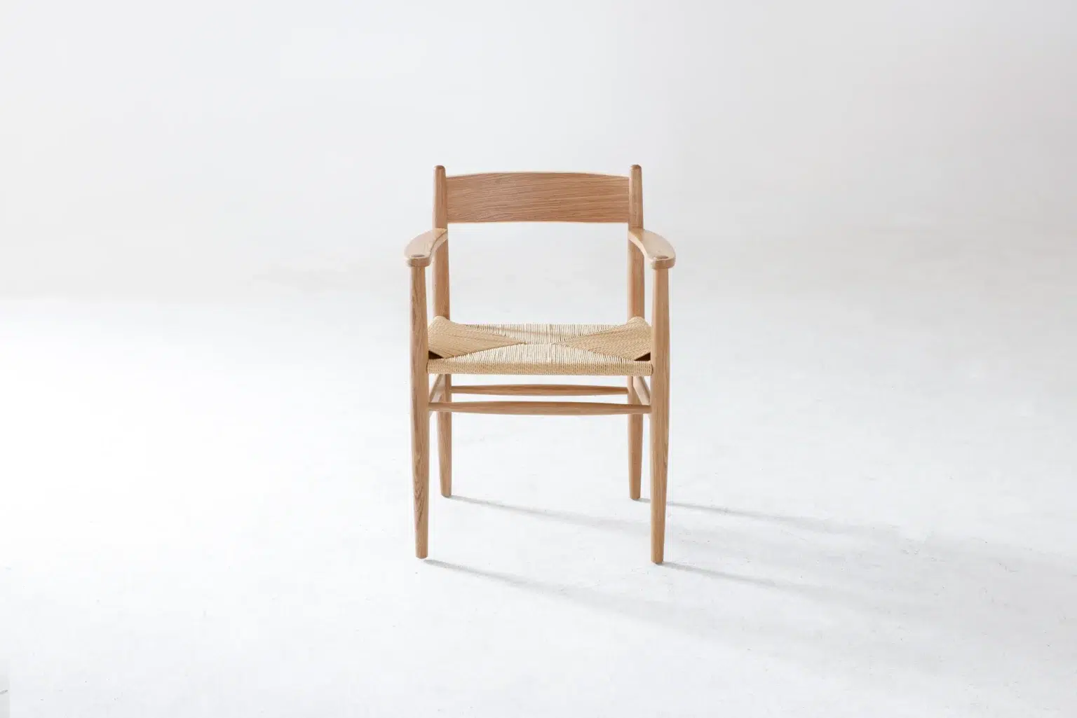 Front view A wooden chair with a woven seat and armrests is centred on a plain white background, casting a soft shadow on the floor.
