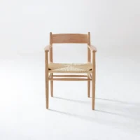 A wooden chair with a woven seat and armrests is centred on a plain white background, casting a soft shadow on the floor.