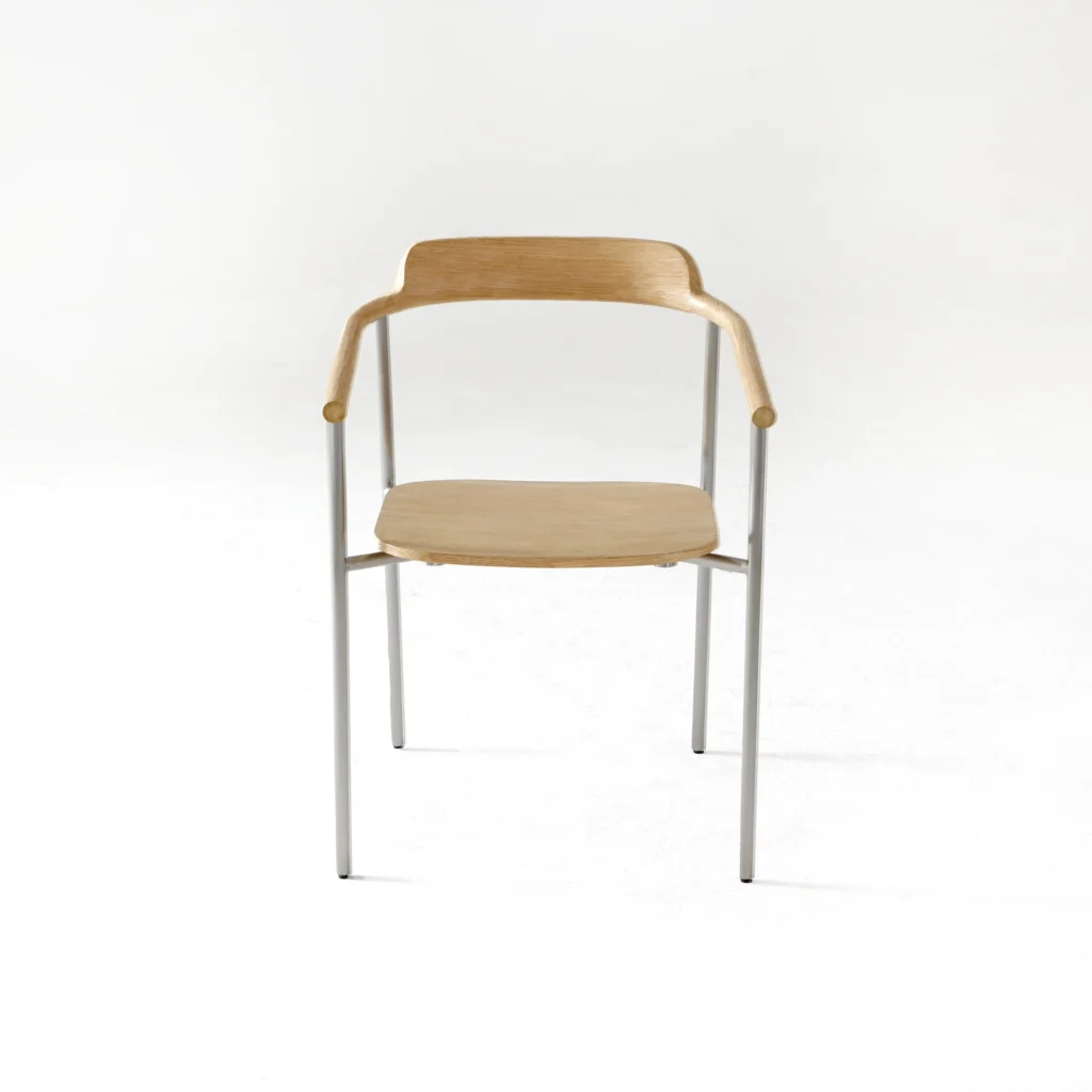 A minimalist chair with a light wooden seat, backrest, and armrests, supported by slender metal legs, is shown against a plain white background.