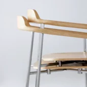 A close-up of two modern stackable wooden chairs with light wood seats and backs, supported by metal legs, against a plain light grey background.