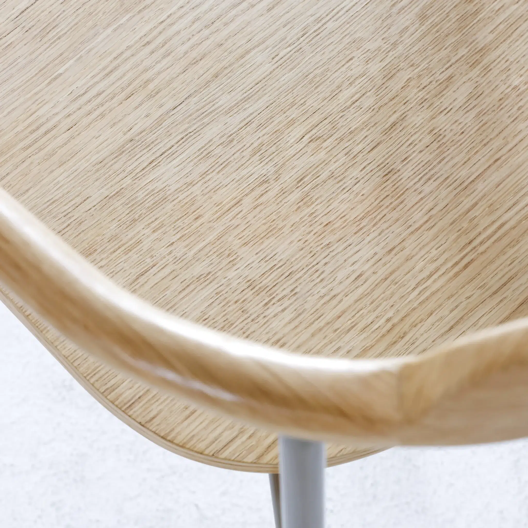 Close-up of a light wooden chair seat with smooth, rounded edges and metal legs, showcasing the natural wood grain and minimalist design.