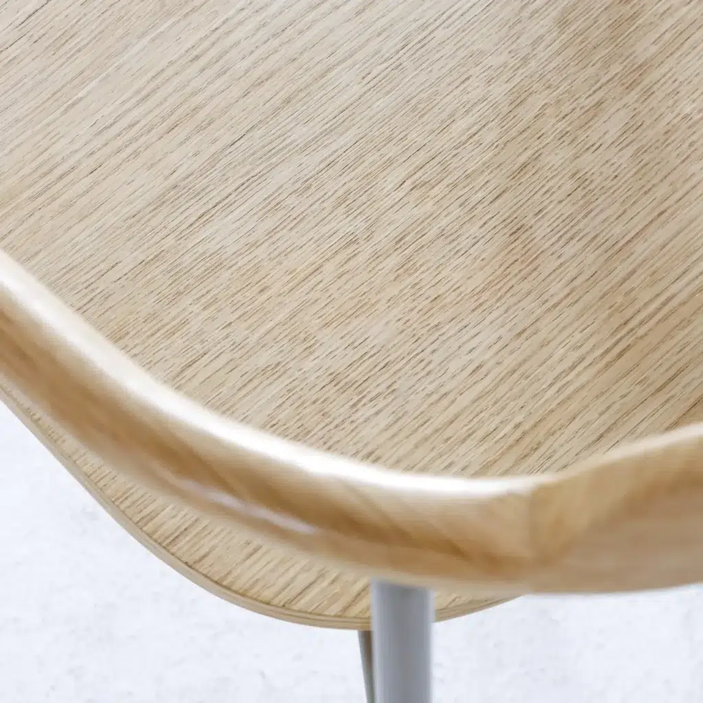 Close-up of a light wooden chair seat with smooth, rounded edges and metal legs, showcasing the natural wood grain and minimalist design.