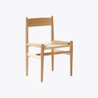 A minimalist wooden chair with a natural finish, featuring a woven seat and a simple, rectangular backrest.