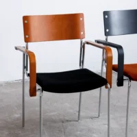 Two modern chairs with metal legs and arms; one has a brown wooden backrest and armrests with a black seat, the other has a black backrest with brown armrests and a black seat, both placed on a concrete floor.
