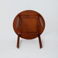 A wooden round table turned upside down, showing its legs and underside against a plain white background.