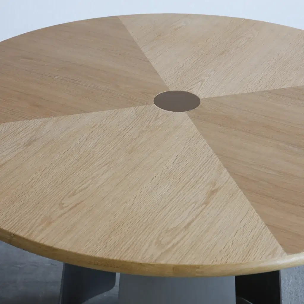 A round wooden table with a geometric pattern of alternating light and medium wood grain sections, featuring a small circular accent at the centre.