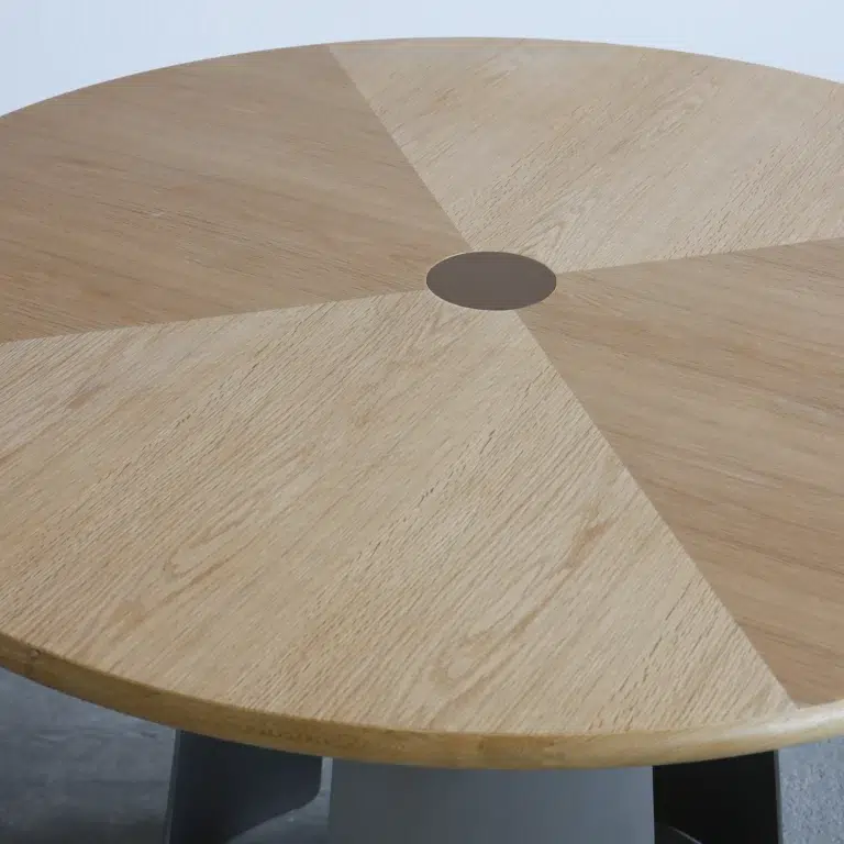 A round wooden table with a geometric pattern of alternating light and medium wood grain sections, featuring a small circular accent at the centre.