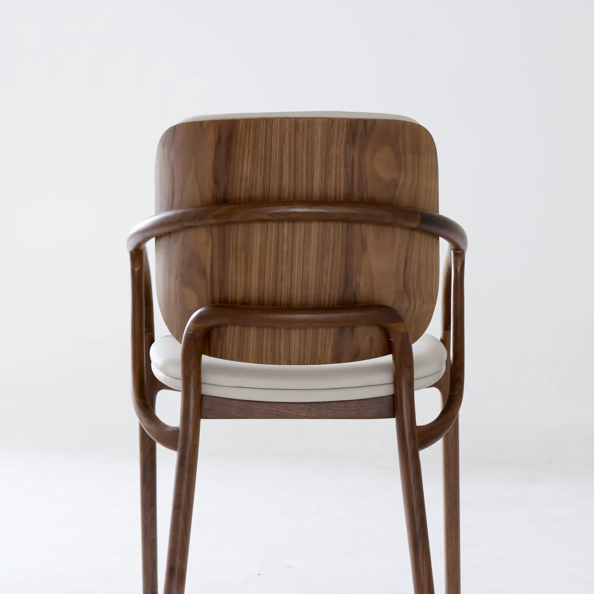 A modern wooden chair with a curved backrest and armrests, featuring a white cushioned seat, is photographed against a plain white background.